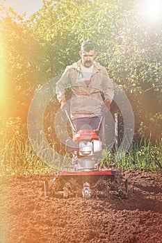 Farmer plows the land with a cultivator, preparing it for planting vegetables, on a sunny day garden