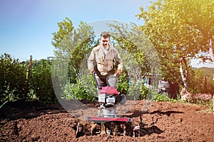 Farmer plows the land with a cultivator, preparing it for planting vegetables, on a sunny day garden