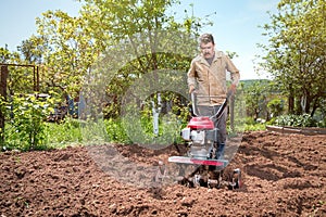 Farmer plows the land with a cultivator, preparing it for planting vegetables, on a sunny day garden