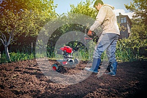 Farmer plows the land with a cultivator, preparing it for planting vegetables, on a sunny day garden