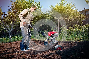 Farmer plows the land with a cultivator, preparing it for planting vegetables, on a sunny day garden