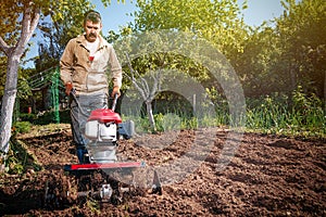 Farmer plows the land with a cultivator, preparing it for planting vegetables, on a sunny day garden