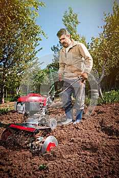 Farmer plows the land with a cultivator, preparing it for planting vegetables, on a sunny day garden