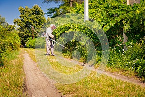 Farmer in protective clothing is mowing grass in garden with manually lawn trimmer
