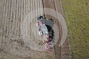 A farmer on a red tractor with a seeder sows grain in plowed land in a private field in the village area. Mechanization of spring