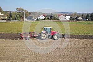 A farmer on a red tractor with a seeder sows grain in plowed land in a private field in the village area. Mechanization of spring