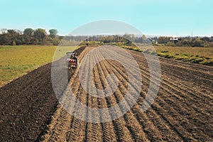 A farmer on a red tractor with a seeder sows grain in plowed land in a private field in the village area. Mechanization of spring