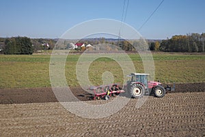 A farmer on a red tractor with a seeder sows grain in plowed land in a private field in the village area. Mechanization of spring