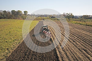 A farmer on a red tractor with a seeder sows grain in plowed land in a private field in the village area. Mechanization of spring