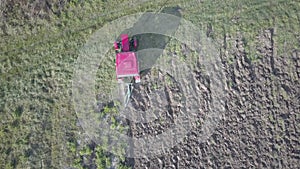 A farmer on a red tractor with a seeder sows grain in plowed land in a private field in the village area. Mechanization of spring