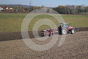 A farmer on a red tractor with a seeder sows grain in plowed land in a private field in the village area. Mechanization of spring