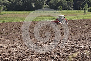 A farmer on a red tractor with a seeder sows grain in plowed land in a private field in the village area. Mechanization of spring