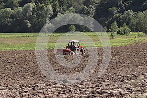 A farmer on a red tractor with a seeder sows grain in plowed land in a private field in the village area. Mechanization of spring