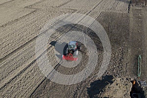 A farmer on a red tractor with a seeder sows grain in plowed land in a private field in the village area. Mechanization of spring