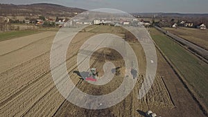 A farmer on a red tractor with a seeder sows grain in plowed land in a private field in the village area. Mechanization of spring