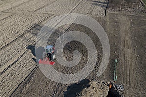 A farmer on a red tractor with a seeder sows grain in plowed land in a private field in the village area. Mechanization of spring