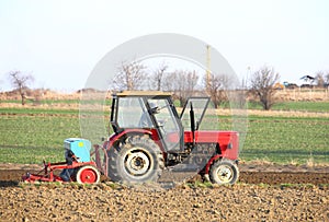 A farmer on a red tractor with a seeder sows grain in plowed land in a private field in the village area. Mechanization of spring