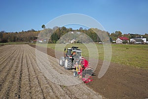 A farmer on a red tractor with a seeder sows grain in plowed land in a private field in the village area. Mechanization of spring