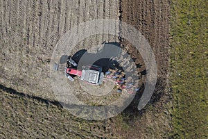 A farmer on a red tractor with a seeder sows grain in plowed land in a private field in the village area. Mechanization of spring