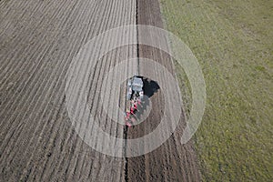 A farmer on a red tractor with a seeder sows grain in plowed land in a private field in the village area. Mechanization of spring
