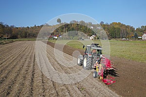 A farmer on a red tractor with a seeder sows grain in plowed land in a private field in the village area. Mechanization of spring