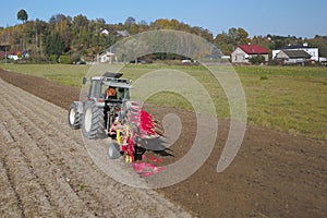 A farmer on a red tractor with a seeder sows grain in plowed land in a private field in the village area. Mechanization of spring