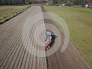 A farmer on a red tractor with a seeder sows grain in plowed land in a private field in the village area. Mechanization of spring