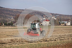 A farmer on a red tractor with a seeder sows grain in plowed land in a private field in the village area. Mechanization of spring