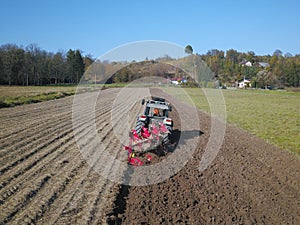 A farmer on a red tractor with a seeder sows grain in plowed land in a private field in the village area. Mechanization of spring