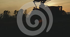 Farmer riding a farm tractor clearing residue crop plants on agriculture field in sunset