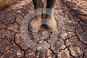 Farmer in rubber boots standing on dry soil ground photo