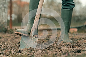 Farmer in rubber boots using spade gardening equipment in garden