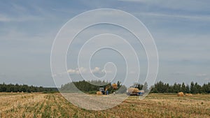 Farmer`s tractor with haystack loads bale of hay into the trailer near ranch, agriculture