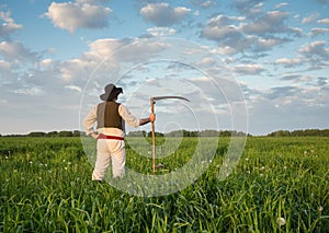 Farmer with a scythe on green field