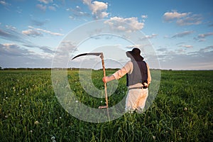 Farmer with a scythe on green field