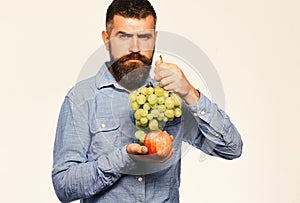 Farmer shows his harvest. Winegrower with strict face holds grapes and red fruit.