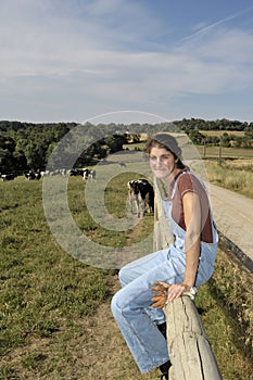 Farmer sitting on a fence and behind her herd of cows photo
