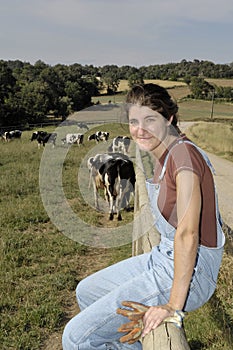 Farmer sitting on a fence and behind her herd of cows