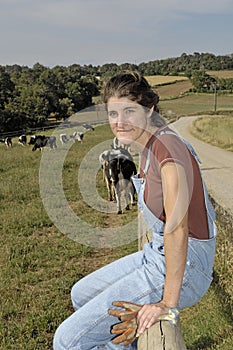 Farmer sitting on a fence and behind her herd of cows photo