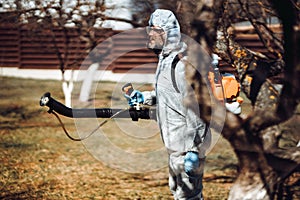 farmer spraying pesticide and insecticide in orchard wearing protective clothing
