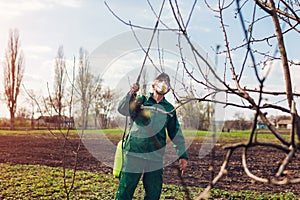 Farmer spraying tree with manual pesticide sprayer against insects in autumn garden. Agriculture and gardening