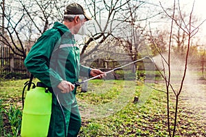 Farmer spraying tree with manual pesticide sprayer against insects in spring garden. Agriculture and gardening