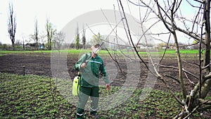 Farmer spraying tree with manual pesticide sprayer against insects in spring garden. Agriculture and gardening