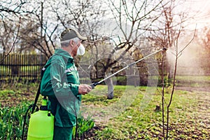 Farmer spraying tree with manual pesticide sprayer against insects in spring garden. Agriculture and gardening