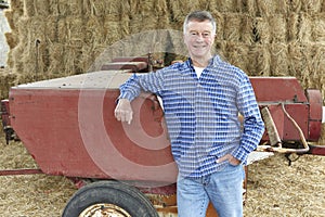 Farmer Standing In Front Of Bales And Old Farm Equipment