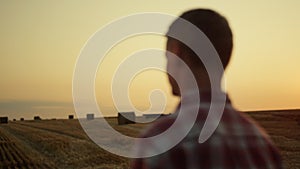 Farmer standing haystack field golden sunset back view. Agriculture concept