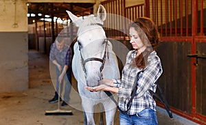 Farmer standing with horse, man cleaning floor at stabling