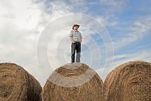 Farmer standing on a huge hay bale under a summer sky.