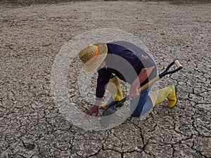 farmer with a straw hat kneeling on the dry, cracked ground. Arid terrain