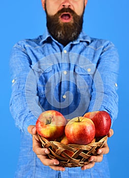 Farmer with surprise on face holds red apples, close up.